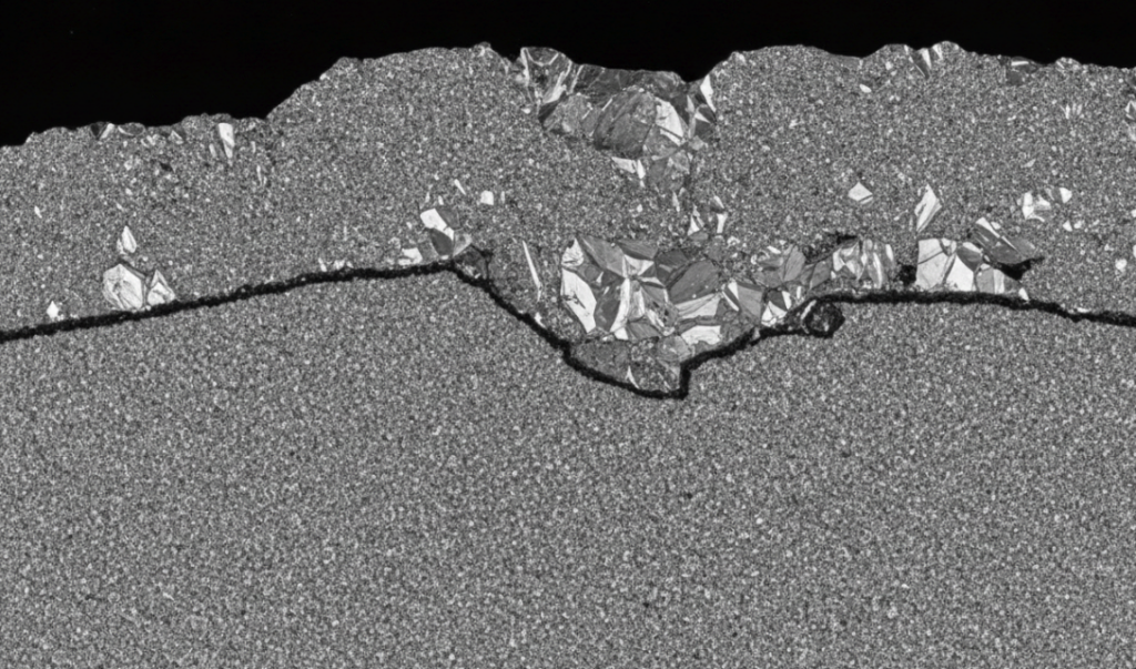an extreme close-up cross-section image showing the boundary layer between the diamond table and the tungsten carbide substrate here.